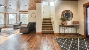 Amplia sala de estar con piso de madera, una escalera y vistas al exterior a través de grandes ventanales.