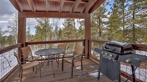 A covered outdoor area with a grill, metal chairs, and a table. - Big Pine Lodge – Rustic charm, hot tub, pet friendly, and room for 12 near Terry Peak! (Lead)
