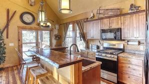 A rustic kitchen with wooden cabinets, a large island, and a hanging deer head. - Big Pine Lodge – Rustic charm, hot tub, pet friendly, and room for 12 near Terry Peak! (Lead)