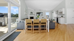 A spacious living area with a dining table, chairs, and a sofa. There is a kitchen area with cabinets and a fireplace. - 5BR w/ Pool, Hot Tub, Cabana, Elevator & Game Rm (Brigantine)