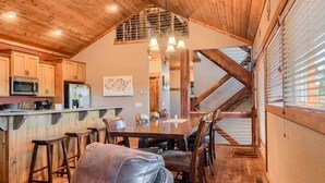A spacious kitchen with wooden cabinets, a dining area with a large table and chairs, and a high ceiling with exposed beams. - Alpine Escape (Lead)