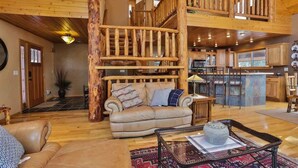 A spacious living area with a high wooden ceiling, a cozy sofa, a coffee table, and a staircase leading to an upper level. - Deep Snow Trail Lodge (Lead)