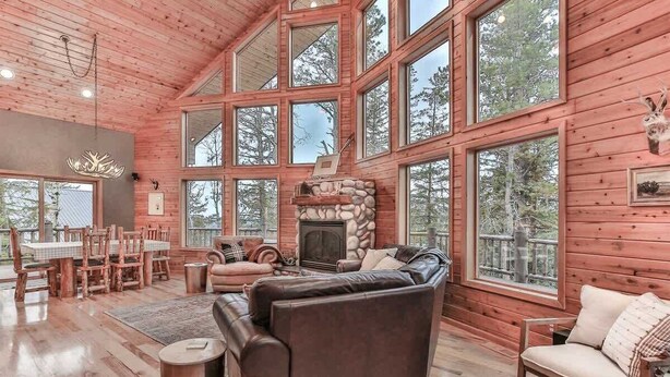 A spacious living room with a fireplace, large windows, and wooden floors. - Deep Snow Trail Lodge (Lead)