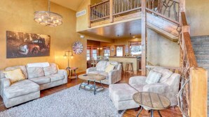 A spacious living area with a high ceiling, a wooden staircase, and a large painting on the wall. - Gunstock Lodge (Lead)