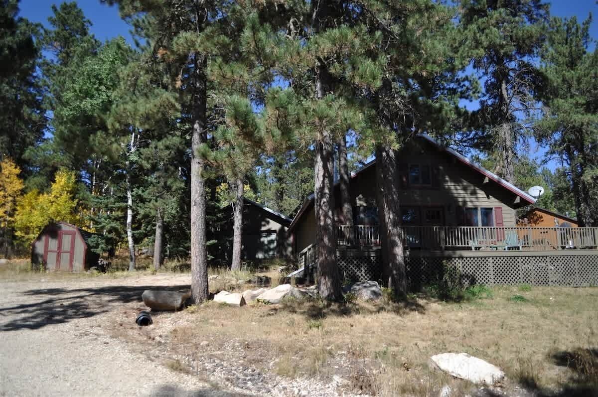 Een chalet met terras, omgeven door bomen en een kleine schuur.