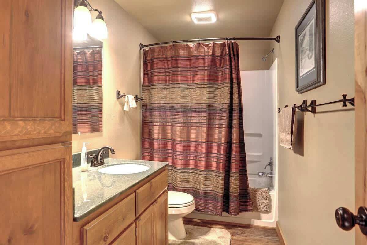 A bathroom with a wooden vanity, a sink, a toilet, a shower with a striped curtain, and a framed picture on the wall.