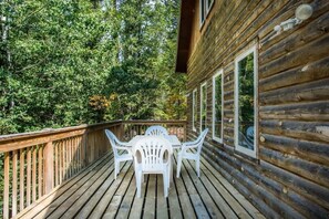 Une terrasse en bois avec une table et des chaises, entourée d’arbres.