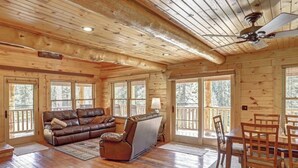 A log cabin interior with a wooden ceiling, a leather sofa, a dining table with chairs, and large windows. - Eagle`s Lair (Lead)