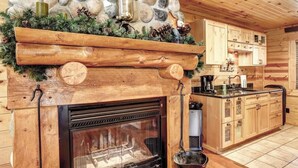 A rustic kitchen with a stone fireplace, wooden cabinets, and a stone wall. - Eagle`s Lair (Lead)