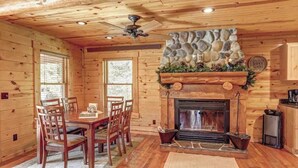 A wooden cabin interior with a stone fireplace, dining table, chairs, and a ceiling fan. - Eagle`s Lair (Lead)