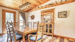 Une table à manger en bois, des chaises, un lustre et un buffet aux portes vitrées.