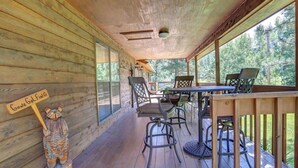 Une terrasse en bois avec une table et des chaises, un panneau en bois et une vue sur les arbres.