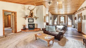 Un salon spacieux avec un plafond en bois, une cheminée, une grande tête de cerf décorative et un coin salon confortable.