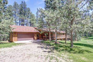 A single-story wooden cabin with a garage, surrounded by pine trees and a grassy yard. - Chase`s cabin by the creek (Lead)