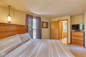 A bedroom with a wooden headboard, a bed with patterned bedding, a television on a wooden dresser, and a door leading to a bathroom. - Chase`s cabin by the creek (Lead)