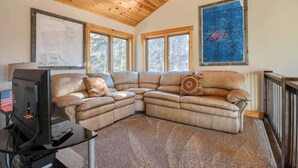 A living room with a sectional sofa, a television, and two large windows. - Triple R Retreat – Hot Tub, Loft & Black Hills Views (Lead)