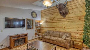 Un salon avec un mur en bois, une tête de taureau fixée au mur, un canapé, une table basse et un téléviseur.