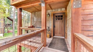 Una cabaña de madera con un porche, una puerta y un pequeño espacio exterior con un banco y un comedero para pájaros.