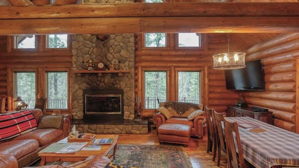 A log cabin interior with a stone fireplace, leather furniture, and a television. - Bear Butte Gulch Lodge - Private cabin with gorgeo (Deadwood)
