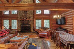 L’intérieur d’une cabane en rondins, avec une cheminée en pierre, des meubles en cuir et un téléviseur.