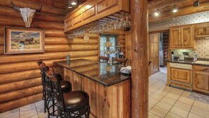 A rustic log cabin interior with a bar area, wooden bar stools, and a kitchen with wooden cabinets. - Bear Butte Gulch Lodge - Private cabin with gorgeo (Deadwood)