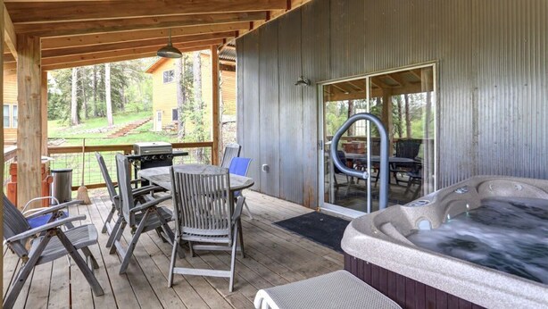 A covered patio with a hot tub, outdoor seating, and a view of a forested area. - Mountain Oasis - private hot tub and game room. (Lead)