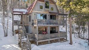Une cabane en rondins à plusieurs étages, dotée d’un balcon et d’un escalier menant à l’entrée.