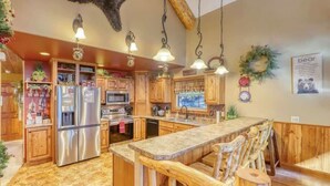 A kitchen with wooden cabinets, stainless steel appliances, and a central island with stools. - Rocky Ridge Lodge – A Black Hills Escape for Family & Friends! (Lead)