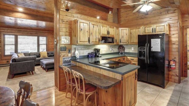 A log cabin interior with a kitchen featuring wooden cabinets, a black refrigerator, and a bar area. - Whispering Grace Retreat (Rapid City)