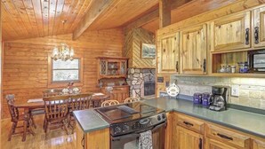 A wooden cabin interior with a dining area, kitchen, and a stone fireplace. - Whispering Grace Retreat (Rapid City)