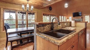 Interior de uma cabana de madeira com cozinha, bancadas de granito, pia e área de refeições com bancos.