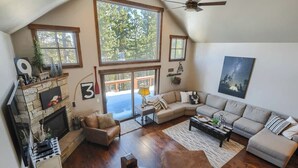 A spacious living room with a fireplace, large windows, a ceiling fan, and a cozy seating area.