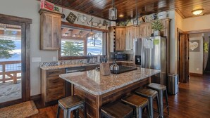 A kitchen with wooden cabinets, a granite island with bar stools, stainless steel appliances, and a view of the outdoors.