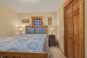 Une chambre à coucher avec un lit, des lampes de chevet, une armoire en bois et un rideau à carreaux.