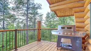 A wooden deck with a grill and a view of a forest. - Dakota Log Cabin – Rustic charm, amazing views, wildlife watching & cozy family spaces! (Lead)