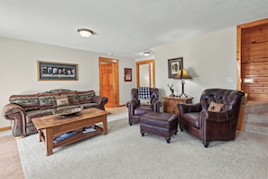 A living room with a sofa, armchairs, a coffee table, a fireplace, and a wooden door.