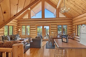 A log cabin interior with a dining area, a sofa set, and a kitchen counter.