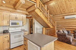 A kitchen with wooden cabinets, a microwave, an oven, and a dishwasher. There is a wooden staircase with a railing.