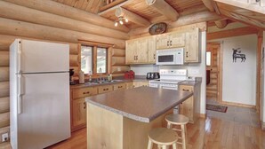 A log cabin kitchen with wooden cabinets, a refrigerator, a microwave, and a large island with stools. - Dakota Log Cabin – Rustic charm, amazing views, wildlife watching & cozy family spaces! (Lead)