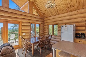 A log cabin with a dining area, kitchen, and large windows.