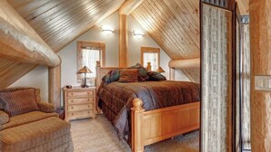 A cozy attic bedroom with a wooden ceiling, a large bed with a wooden headboard, a dresser, and a chair. - Dakota Log Cabin – Rustic charm, amazing views, wildlife watching & cozy family spaces! (Lead)