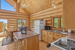 A log cabin with a kitchen featuring a refrigerator, coffee maker, and a dining area with chairs and a table.