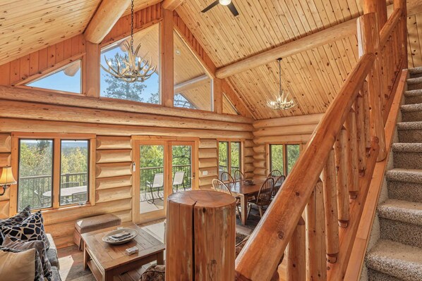 L’intérieur d’une cabane en rondins comprend un coin repas, un escalier et une grande fenêtre donnant sur l’extérieur.