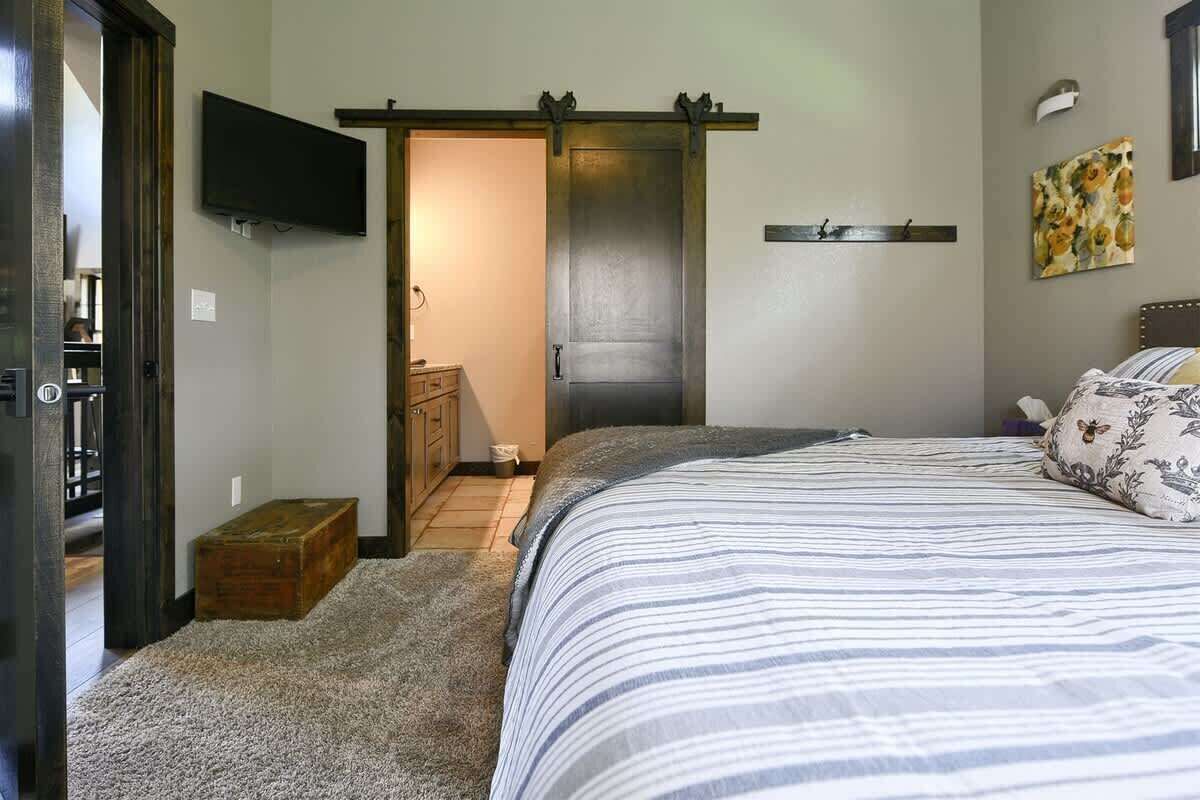 A bedroom with a bed, a television mounted on the wall, a door, and a small wooden chest.