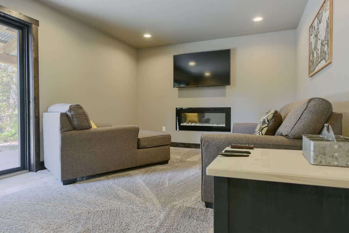 A modern living room with two sofas, a flat-screen TV mounted on the wall, and a large window providing natural light.