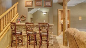 Zona de bar con tres taburetes de madera y un fondo de pared de piedra.