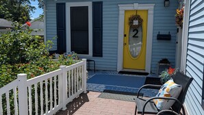A house with a yellow door, number 2, a porch with a white railing, and a brick patio. - Cozy, Cute, Private Ozark Suite 5 Mins to Hospital (Ozark)