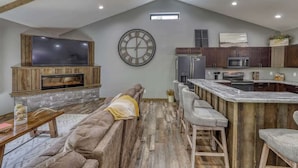 Un espacio habitable tipo loft con chimenea de piedra, un gran reloj de pared y una cocina con electrodomésticos modernos.