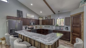 Una cocina moderna con una isla central, electrodomésticos integrados y un techo de madera rústica.