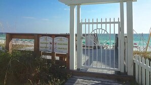 Een omheind toegangspoortje naar het strand, met een pergola en borden met informatie over activiteiten op het strand.